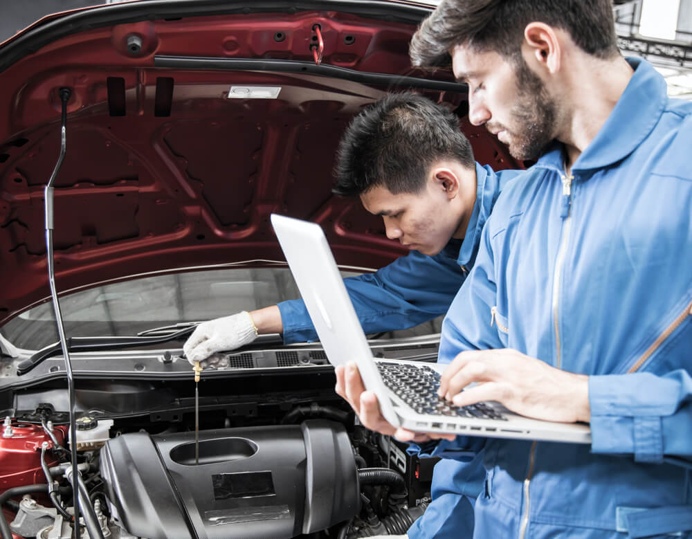 automotive technician checking shop's online reputation on a laptop while car is being fixed